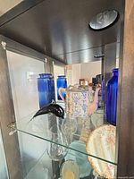 Shelf with cobalt bottles, teapot, black glass figurine, stemless glasses, floral plate