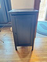 Front view of black engineered wood nightstand with closed door and four legs