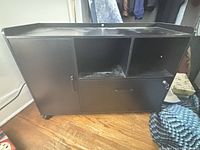 Front view of black engineered wood TV stand showing cabinet door, open shelf, drawer, and casters