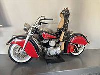 Full view of red and black Indian motorcycle model with wooden cat rider on stand