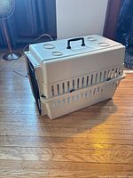 Side view of beige plastic pet carrier showing handle, ventilation slots, and assembled halves