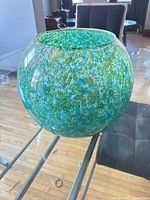side view of mottled green/turquoise/blue glass fishbowl vase on glass table