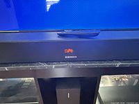 Front view of soundbar beneath TV with remote on top; LED display lit