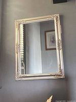 Full view of rectangular silver ornate mirror mounted vertically on wall