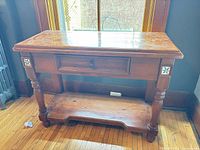 Front view of wooden console table showing tile inlays, drawer, turned legs and lower shelf