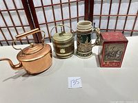 Group shot of all four items: copper kettle, wood/brass biscuit barrel, German stein, red tin