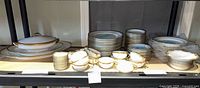 Full set on shelving showing plates, bowls, cups, serving pieces
