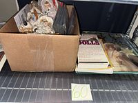 Box of bagged miniature dolls and two books on shelf