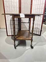 Front view of walnut drop-leaf serving cart with leaves partly extended, showing casters and lower shelf.