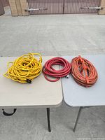 Coiled yellow extension cord, red air hose and orange multi-outlet power cord on tables