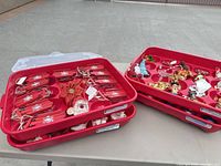 Three red plastic trays holding assorted ornaments including wooden sleds, glass baubles, figurines
