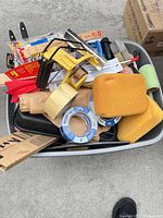 Overview of tote with assorted painting supplies: sponges, tape rolls, roller frame, sanding sheets, edger