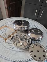Cookware components laid out: base pan, two lids, 6-cup insert, steamer plate, metal stand