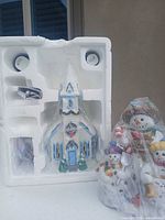 Styrofoam insert holding porcelain church and wrapped snowman trio figurine