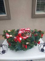 Overall view of faux pine centerpiece with red and gingham ribbons, pinecones, berries, dried fruit slices, and two metal candle holders