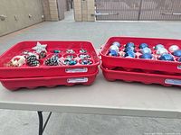 Four red compartment trays on table, two open showing assorted ornaments, two open showing blue and silver baubles
