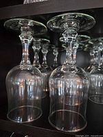 four clear tall wine glasses inverted on shelf