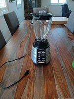 Front view of Oster countertop blender with glass jar, black lid, power cord, stainless steel control base on wooden table