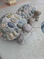 Two concrete turtle statues with river stone shells on poolside ledge