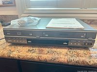 Front view of combo player with remote in bag and manual on top