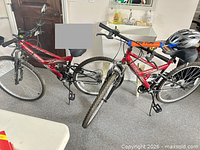 Both red mountain bikes standing side by side showing full view and helmet on handlebar