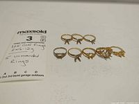 overall view of eight unmounted gold ring settings beside handwritten note