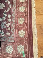 Corner of rug showing burgundy field, teal and cream border motifs, and cream fringe