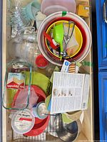 Drawer view showing nested plastic bowls, glass loaf pan, measuring cups, silicone liners, dishers, utensils