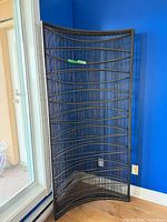 Full view of curved bronze metal room divider against blue wall