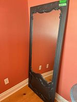 Front angled view of tall ornate black mirror leaning against wall