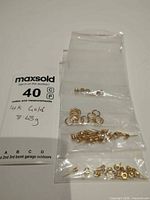 Four small bags containing assorted 14K yellow gold pieces next to weight note