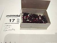 Box containing numerous oval deep red garnet cabochons