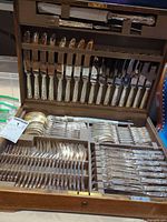 Open wooden flatware chest showing knives, forks, spoons, serving pieces in fitted slots