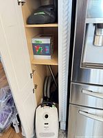 Cabinet shelf showing Miele white canister vacuum, hose, wand, and floorhead plus boxed filter bags