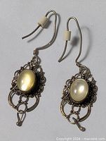 Full view of both earrings showing filigree design, moonstone cabochons, hooks and silicone stoppers