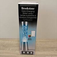 Front of boxed Brookstone color-changing glitter lamp showing product image and branding