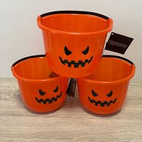 Front view of three orange pumpkin pails showing face graphics