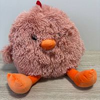Front view of round pink plush chicken with orange beak and feet, red comb