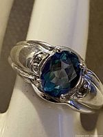 Ring close-up showing blue-teal gemstone and white gold setting