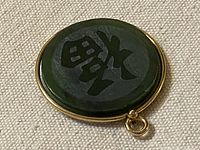 Front view of green jade pendant with Fu character and gold-filled bezel