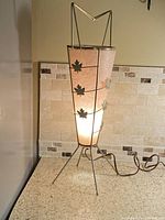Full view of lamp lit, showing metal frame, fiberglass shade, maple leaf accents, cord and plug