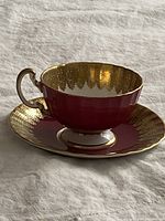 Teacup on saucer showing deep red glaze and gold filigree border