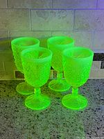 Four small uranium glass goblets glowing green under UV light