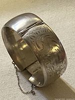 Full view of sterling silver hinged cuff showing engraving and safety chain