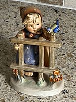 Front view of porcelain figurine girl behind fence with bird