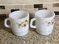 Pair of white milk glass mugs showing front floral butterfly decals and handles
