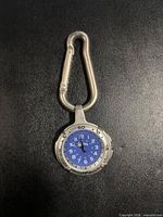 Front view of watch attached to carabiner showing blue dial and bezel