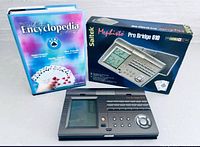 Front view of hardcover encyclopedia, boxed Pro Bridge 610, and handheld unit