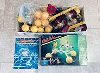 Top view of open box showing yellow spheres, red wheels, clear capsules, yellow beams; Capsela booklet and Capsela 400 box front