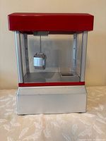 Front view of red and silver claw machine, claw visible inside